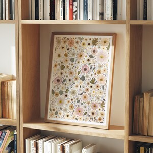 May include: A rectangular framed print featuring a dense, repeating pattern of pressed flowers in shades of soft pink, cream, muted yellow, and sage green. The artwork is encased in a light-toned wooden frame and displays a variety of botanical shapes.