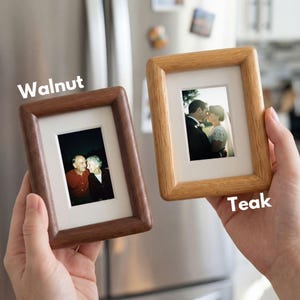 May include: Two rectangular wooden picture frames with white matting. The left frame is dark brown walnut wood containing a photo of two people. The right frame is light brown teak wood containing a wedding photo. The text Walnut and Teak is visible.