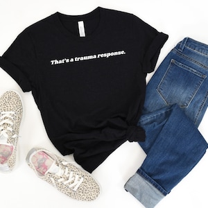 Pode incluir: Camiseta preta com texto branco que diz "That's a trauma response."