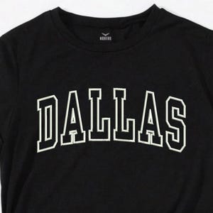 May include: Black t-shirt with white embroidered text that reads "DALLAS".