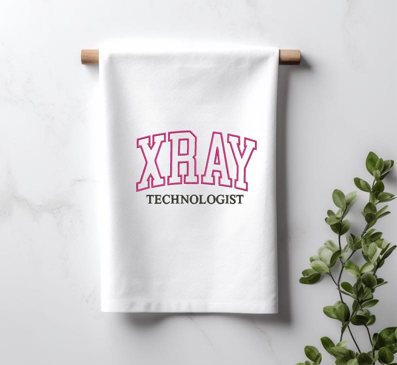 K&ouml;nnte beinhalten: Wei&szlig;es K&uuml;chentuch mit dem Text "XRAY TECHNOLOGIST" in einer pinkfarbenen und wei&szlig;en College-Schrift.