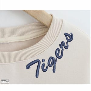 May include: A beige sweatshirt with a navy blue embroidered "Tigers" design on the front.