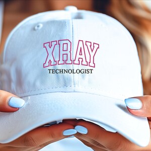K&ouml;nnte beinhalten: Wei&szlig;e Baseballkappe mit rosa gesticktem Text "XRAY TECHNOLOGIST".