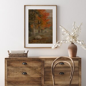 Puede incluir: Una pintura enmarcada que representa una escena de bosque con &aacute;rboles en varios tonos de verde y naranja. Los &aacute;rboles est&aacute;n en primer plano de la pintura, con una ladera en el fondo. La pintura est&aacute; colgada en una pared blanca sobre una c&oacute;moda de madera.