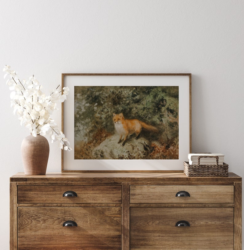 May include: A framed print of a red fox standing on a rock in a forest setting. The fox is looking to the left of the image. The print is in a brown wooden frame.