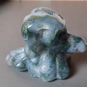 May include: A carved stone sculpture of an octopus. The sculpture is primarily blue-grey with green and white veining throughout. The octopus has a rounded head and tentacles that curl around its body.