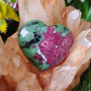 May include: A heart-shaped gemstone with a vibrant color palette. The stone features a mix of green, black, and deep red hues. The polished surface reflects light, highlighting the natural patterns and textures of the stone. This decorative piece is a unique addition to any collection.