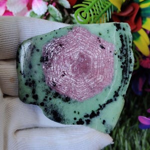 Puede incluir: Una piedra preciosa verde y rosa con un patr&oacute;n de estrella. La piedra tiene una forma irregular y tiene motas negras.
