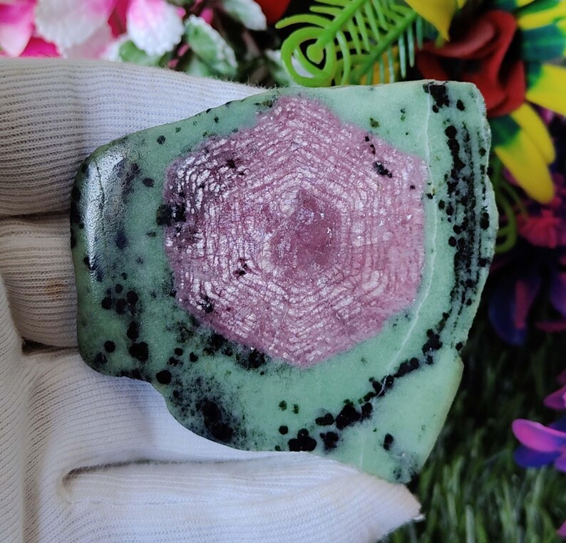 Puede incluir: Una piedra preciosa verde y rosa con un patr&oacute;n de estrella. La piedra tiene una forma irregular y tiene motas negras.