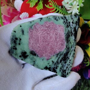 May include: A green and black stone with a pink, hexagonal pattern in the centre. The stone is irregularly shaped and has a rough texture.