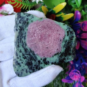 May include: A green and pink gemstone with a starburst pattern. The gemstone is rough and has a natural, unpolished look.