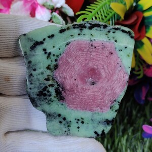 Puede incluir: Una piedra preciosa verde y rosa con inclusiones negras. La piedra preciosa tiene una forma hexagonal y est&aacute; rodeada de una matriz verde.