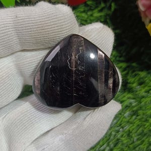 May include: A black heart-shaped stone with silver streaks. The stone is polished and has a smooth surface.