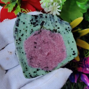 Pu&ograve; includere: Una pietra verde e nera con un centro rosa e nero. La pietra &egrave; grezza e ha un aspetto naturale non levigato.