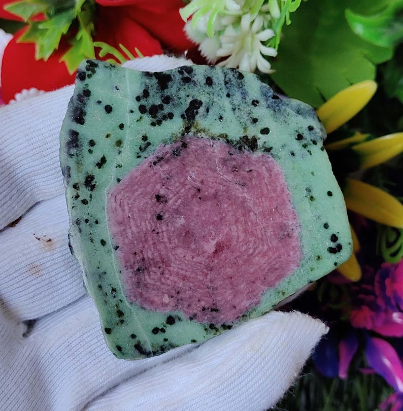 Pu&ograve; includere: Una pietra verde e nera con un centro rosa e nero. La pietra &egrave; grezza e ha un aspetto naturale non levigato.