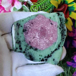 Puede incluir: Una piedra preciosa verde y rosa con un patr&oacute;n de estrella. La piedra preciosa est&aacute; pulida y tiene una superficie lisa.