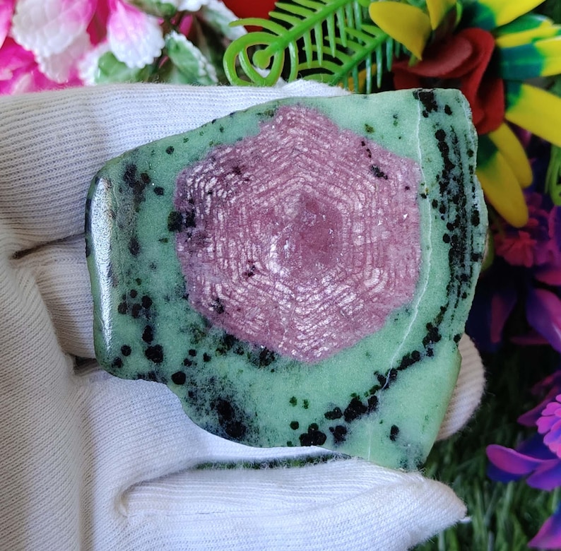 Puede incluir: Una piedra preciosa verde y rosa con un patr&oacute;n de estrella. La piedra preciosa est&aacute; pulida y tiene una superficie lisa.