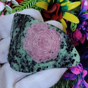 May include: A green and pink gemstone with a starburst pattern. The gemstone is rough and has a natural, unpolished look.