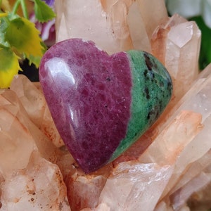 May include: A heart-shaped green and pink gemstone, also known as a ruby zoisite, resting on a bed of white quartz crystals.