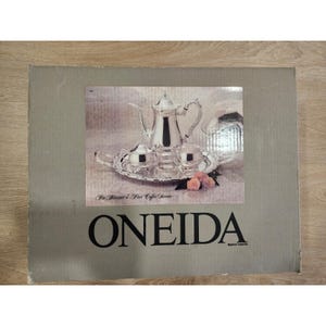 May include: A silver-toned Oneida coffee service set, including a teapot, sugar bowl, creamer, and two cups, presented on a decorative tray. The box features the Oneida logo and the text "In Almond 4-Piece Coffee Service".