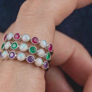 Peut inclure: Une pile de trois bagues en argent, chacune ornée d'une rangée de pierres rondes serties clos. La bague supérieure alterne des pierres rouges et blanches, celle du milieu des vertes et blanches, et l'inférieure des violettes et blanches.