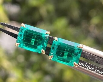 Pode incluir: Um par de brincos de pedra preciosa verde esmeralda com engastes de ouro. Os brincos são segurados por uma pinça com o texto "unique jewelin" visível.