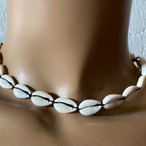 May include: A white shell necklace with black string. The necklace is made of cowrie shells.