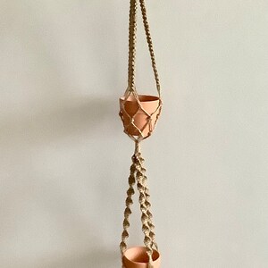 May include: A macrame plant hanger with four terracotta pots hanging from it. The hanger is made of natural twine and has a simple design.