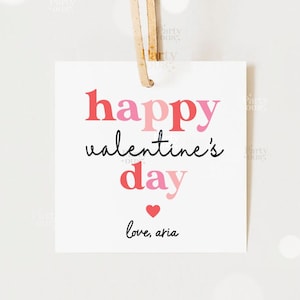 May include: A white gift tag with pink and red text that reads "happy valentine's day" and "love, aria". There is a small red heart above the signature.