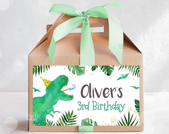 May include: A brown favor box with a green ribbon and a label that says "Oliver's 3rd Birthday". The label features a green dinosaur with a party hat and a party blower. The dinosaur is surrounded by green leaves and gold glitter.