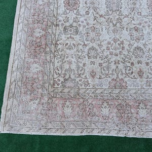 May include: A vintage rug with a floral pattern in shades of pink and white. The rug has a distressed look and a fringe border.