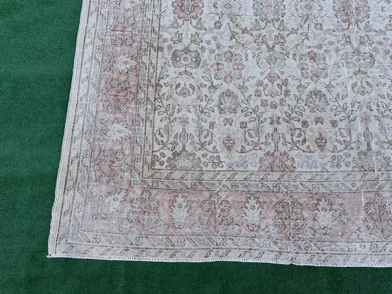 May include: A vintage rug with a floral pattern in shades of pink and white. The rug has a distressed look and a fringe border.