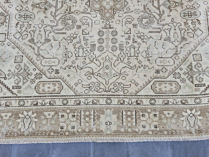 K&ouml;nnte beinhalten: Nahaufnahme eines beige-braunen Teppichs mit Muster. Der Teppich weist ein kompliziertes Design mit floralen und geometrischen Motiven auf. Der Rand ist in einem dunkleren Braunton gehalten und der Teppich hat einen Used-Look.