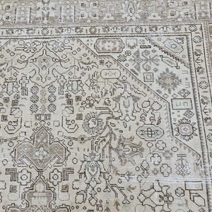 K&ouml;nnte beinhalten: Nahaufnahme eines beige-braunen Teppichs mit Muster. Der Teppich weist ein kompliziertes Design mit floralen und geometrischen Motiven auf. Der Rand ist in einem dunkleren Braunton gehalten, und der Teppich scheint Vintage oder antik zu sein.