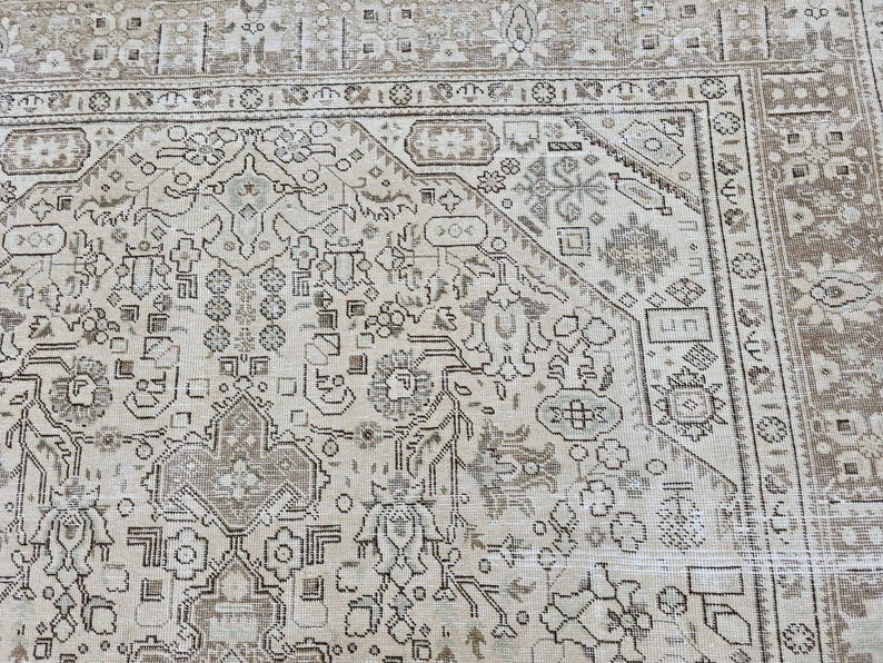K&ouml;nnte beinhalten: Nahaufnahme eines beige-braunen Teppichs mit Muster. Der Teppich weist ein kompliziertes Design mit floralen und geometrischen Motiven auf. Der Rand ist in einem dunkleren Braunton gehalten, und der Teppich scheint Vintage oder antik zu sein.