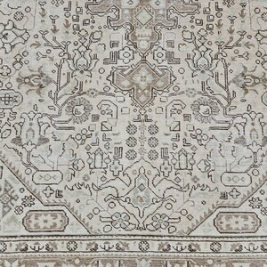 K&ouml;nnte beinhalten: Nahaufnahme eines beige-braunen Teppichs mit Muster. Der Teppich weist ein kompliziertes Design mit floralen und geometrischen Motiven auf. Der Rand ist in einem dunkleren Braunton gehalten, und der Gesamtstil ist Vintage.