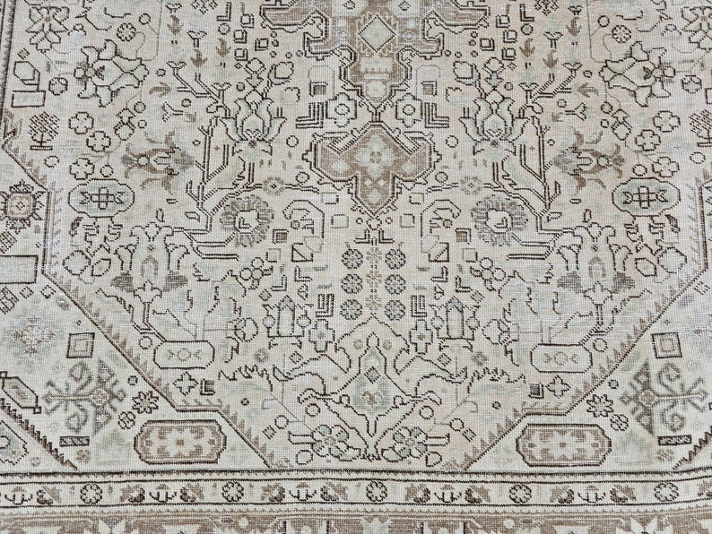 K&ouml;nnte beinhalten: Nahaufnahme eines beige-braunen Teppichs mit Muster. Der Teppich weist ein kompliziertes Design mit floralen und geometrischen Motiven auf. Der Rand ist in einem dunkleren Braunton gehalten, und der Gesamtstil ist Vintage.