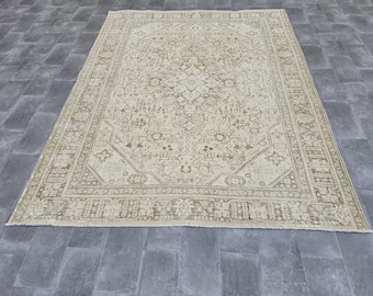 May include: A large, rectangular rug with an intricate, traditional pattern. The rug features a cream-colored background with a detailed design in shades of brown and beige. The border has a repeating geometric pattern.