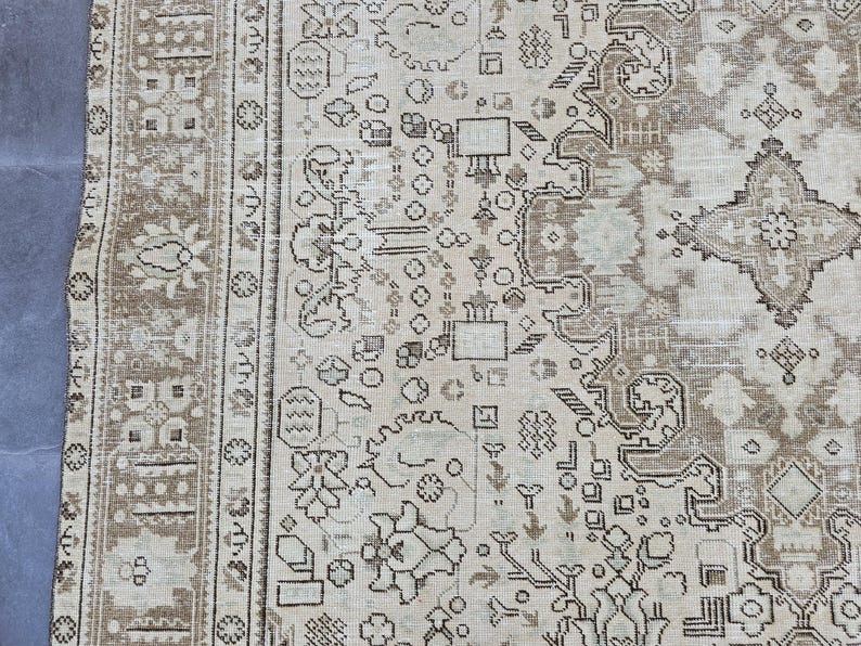 K&ouml;nnte beinhalten: Ein Abschnitt eines beigefarbenen und braunen Vintage-Teppichs mit einem komplizierten, sich wiederholenden Muster. Der Teppich weist florale und geometrische Designs in Beige-, Braun- und Graut&ouml;nen auf. Der Rand hat ein dunkleres braunes Blumenmuster.