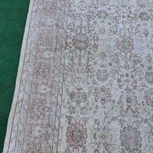 May include: A vintage rug with a floral pattern in shades of beige, brown, and pink. The rug has a border with a repeating design.