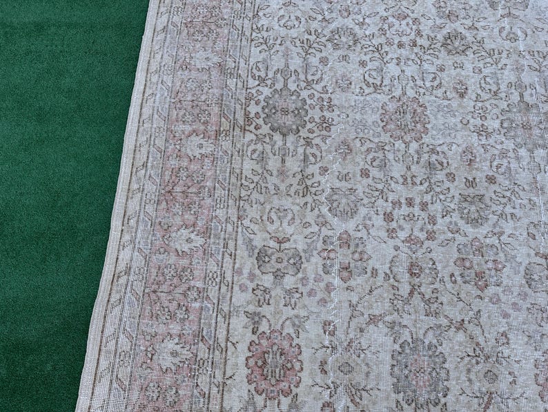 May include: A vintage rug with a floral pattern in shades of beige, brown, and pink. The rug has a border with a repeating design.