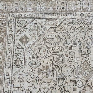 K&ouml;nnte beinhalten: Ausschnitt eines beigefarbenen und braunen Vintage-Teppichs mit einem aufwendigen, sich wiederholenden geometrischen Muster. Der Teppich zeigt ein zentrales Design mit floralen und abstrakten Formen, umrahmt von einem detaillierten Rand. Die Farbpalette ist neutral, mit Beige-, Braun- und Gr&uuml;nt&ouml;nen.