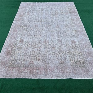 May include: A vintage white rug with a floral pattern and a faded pink border. The rug has a distressed look and is made of a soft, woven material.