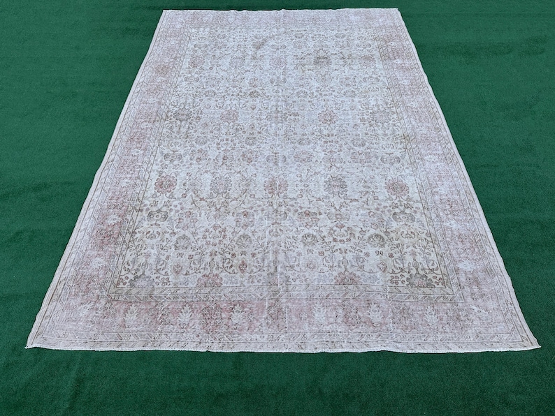 May include: A vintage white rug with a floral pattern and a faded pink border. The rug has a distressed look and is made of a soft, woven material.