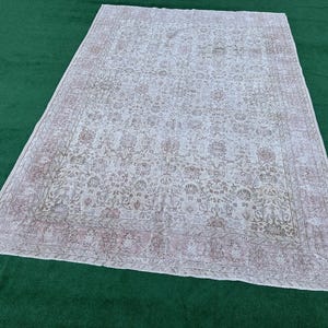 May include: A white vintage rug with a floral pattern and a pink border. The rug has a distressed look and is made of a soft, woven material.