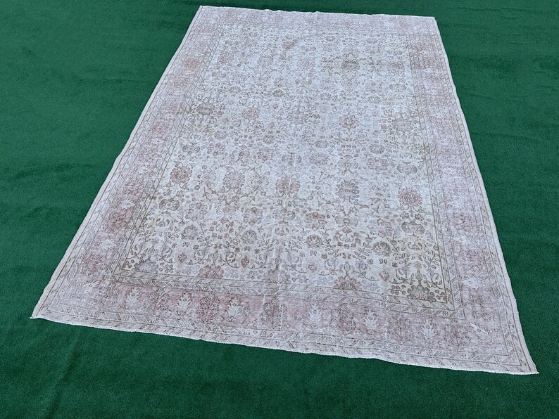 May include: A white vintage rug with a floral pattern and a pink border. The rug has a distressed look and is made of a soft, woven material.