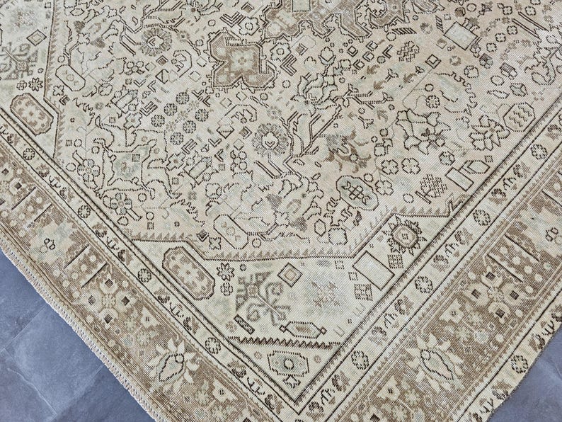 K&ouml;nnte beinhalten: Ein antiker beigefarbener Teppich mit einem detaillierten, komplizierten Muster. Der Teppich hat ein zentrales Design mit floralen und geometrischen Elementen, das von einem braunen Rand umrahmt wird. Die Gesamt&auml;sthetik ist Vintage und klassisch.