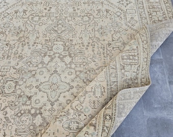 May include: Beige and brown vintage-style area rug with an intricate, repeating geometric pattern. The rug has a distressed look, with a rolled-up section revealing the underside. The design features floral and medallion motifs, creating a classic, elegant aesthetic.