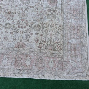 May include: A vintage rug with a faded floral pattern in shades of beige and pink. The rug has a distressed look and a fringed edge.