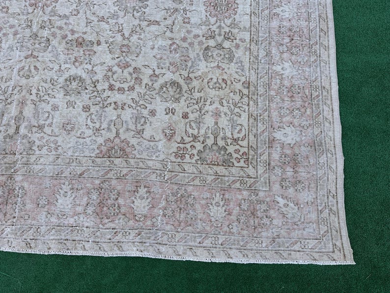 May include: A vintage rug with a faded floral pattern in shades of beige and pink. The rug has a distressed look and a fringed edge.